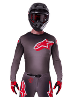 Alpinestars 2025 Supertech Lipan Jersey, motocross-trøje, Smoke og rød, med et stort rødt og hvidt logo på brystet, båret med en sort hjelm og røde og sorte handsker, atletisk race-pasform med laserskårne perforeringer