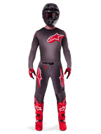 Motocrossrytter iført Alpinestars 2025 Supertech Lipan-udstyrssæt, Smoke og Bright Red, mørkegrå trøje og bukser med markante røde Alpinestars-logoer, klare røde støvler, sort hjelm og røde handsker, koordineret professionelt outfit til terrænkørsel