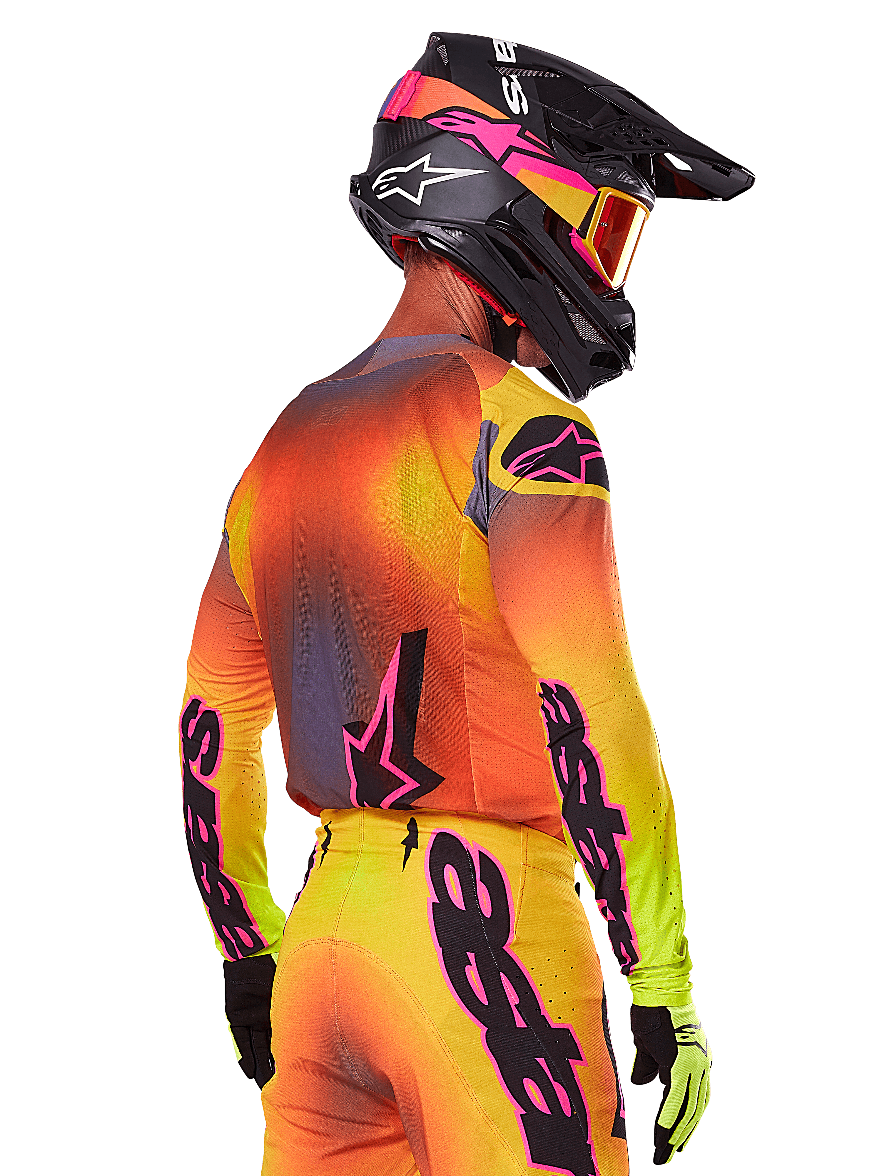 Motocross-kører set bagfra fra siden iført Alpinestars 2025 Supertech Lipan-udstyrssæt, med en gul, orange og rød gradient med sort og lyserød branding, sort hjelm med lyserøde detaljer og orange crossbriller, professionel beklædning til terrænkørsel.