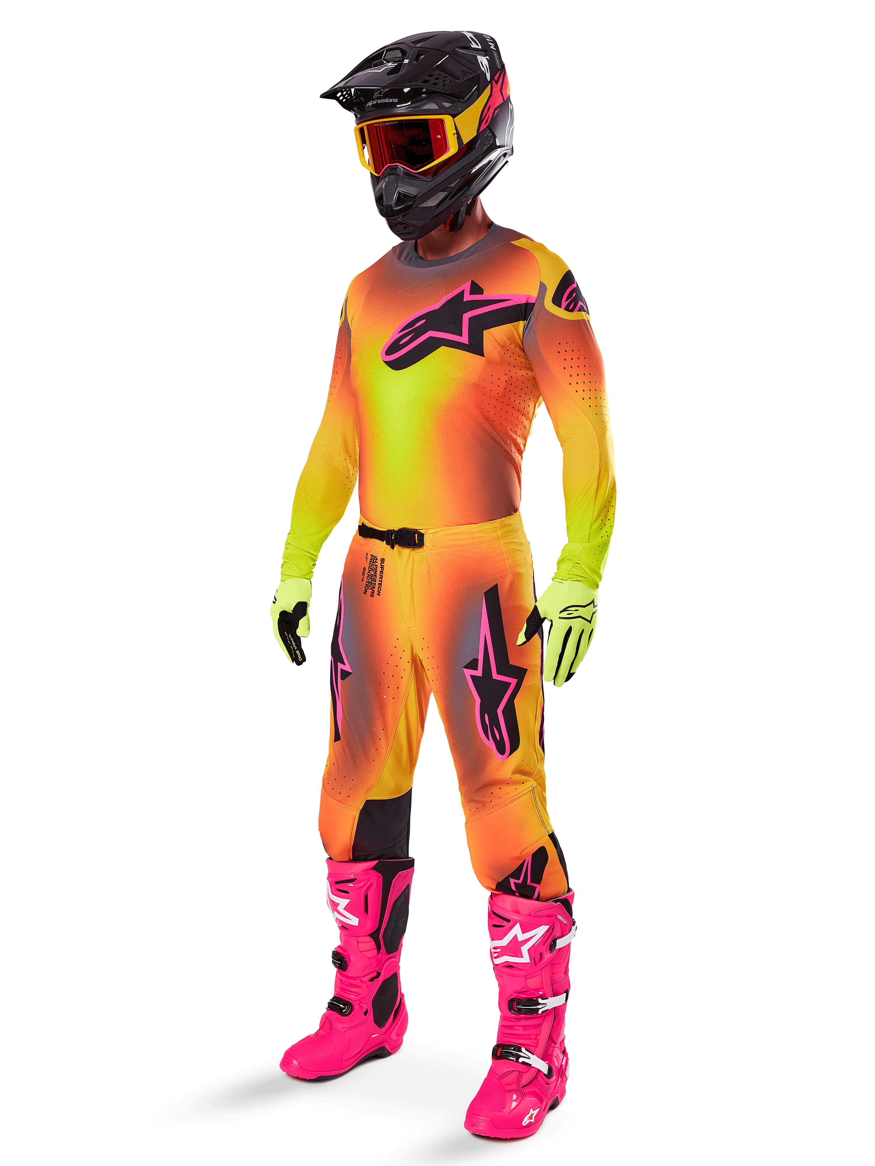 Motocross-kører iført Alpinestars 2025 Supertech Lipan Gear Set, gul og orange trøje og bukser med farveovergang og pink detaljer, sort hjelm med røde og gule goggles, stærke gule handsker og klare pink støvler, koordineret outfit til terrænkørsel