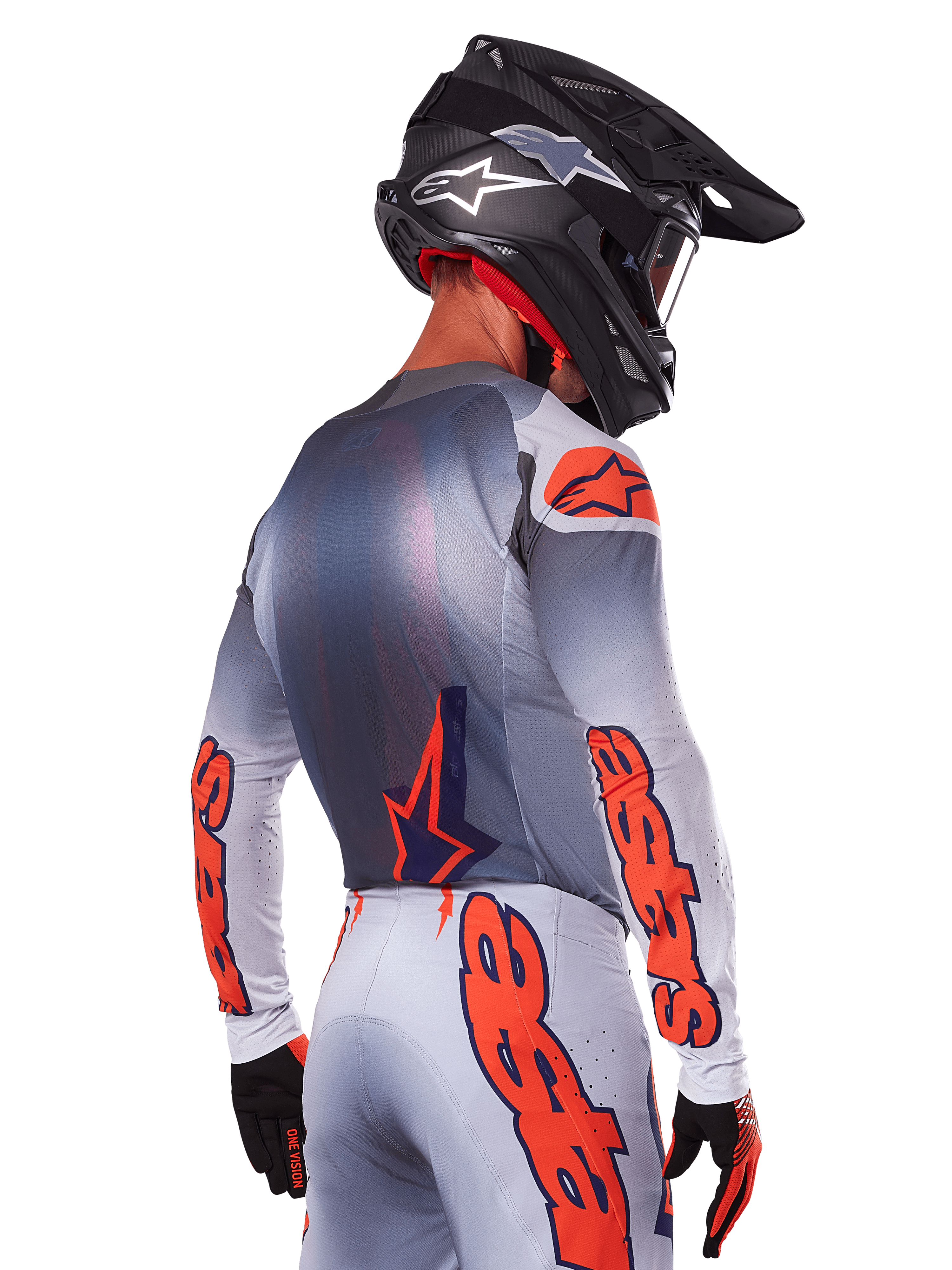 Motocrosskører set bagfra iført Alpinestars 2025 Supertech Lipan jersey og udstyrssæt, grå med orange fluo-detaljer, markant branding på ryg og ærmer, sort hjelm og sorte handsker, koordineret motocross-raceroutfit