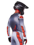 Motocrosskører set bagfra iført Alpinestars 2025 Supertech Lipan-jersey i Gray Orange Fluo, med markante orange logoer på ærmerne og ryggen, kombineret med matchende bukser og en sort hjelm, professionelt racerudstyr til terrænkørsel.