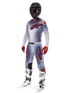 Alpinestars 2025 Supertech Lipan Gear Set, motocross-racerudstyr, grå med fluoriserende orange og mørkeblå stjernegrafik, båret med sort hjelm, røde og sorte handsker og hvid-sorte støvler, komplet professionelt off-road outfit med ventileret design