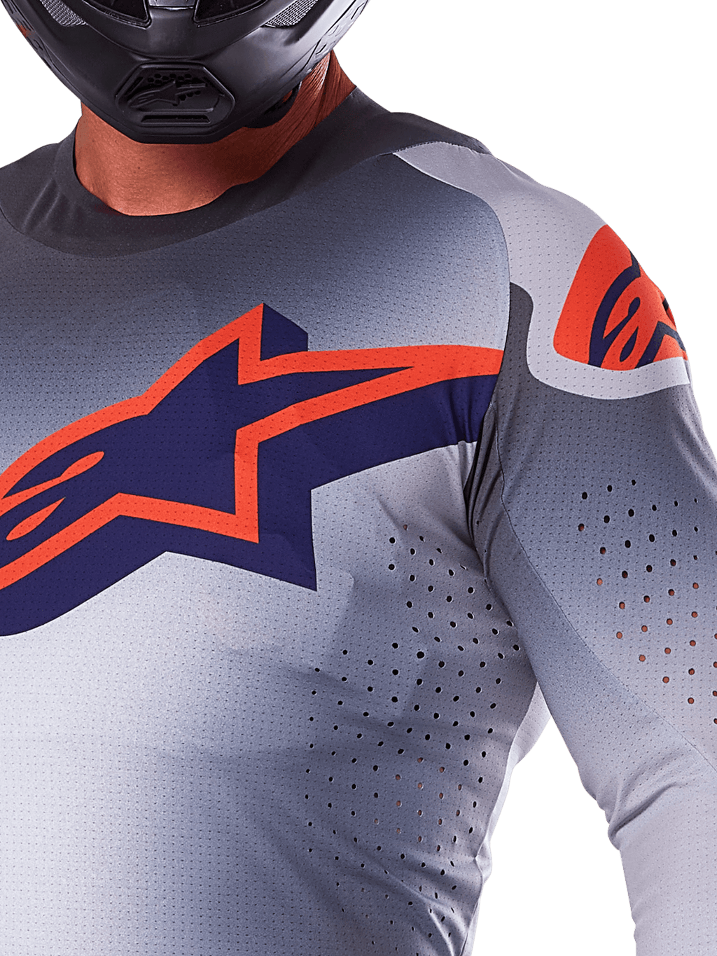 Nærbillede af en kører iført Alpinestars 2025 Supertech Lipan jersey, motocross-trøje, grå og orange fluo, med et stort orange Alpinestars-logo på brystet, laser-skårne ventilationshuller og en sort hjelm, professionelt racerudstyr