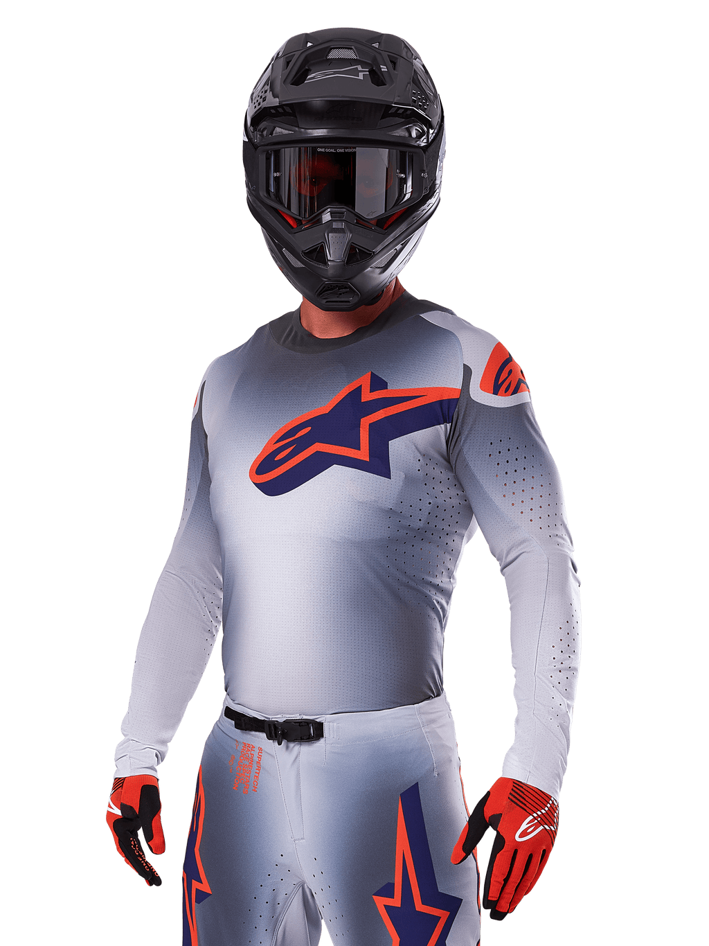 Motocrosskører iført Alpinestars 2025 Supertech Lipan-udstyrssæt, grå jersey og bukser med navy og orange detaljer, mat sort hjelm med goggles og rød-sorte handsker, atletisk præstationsudstyr til terrænkørsel