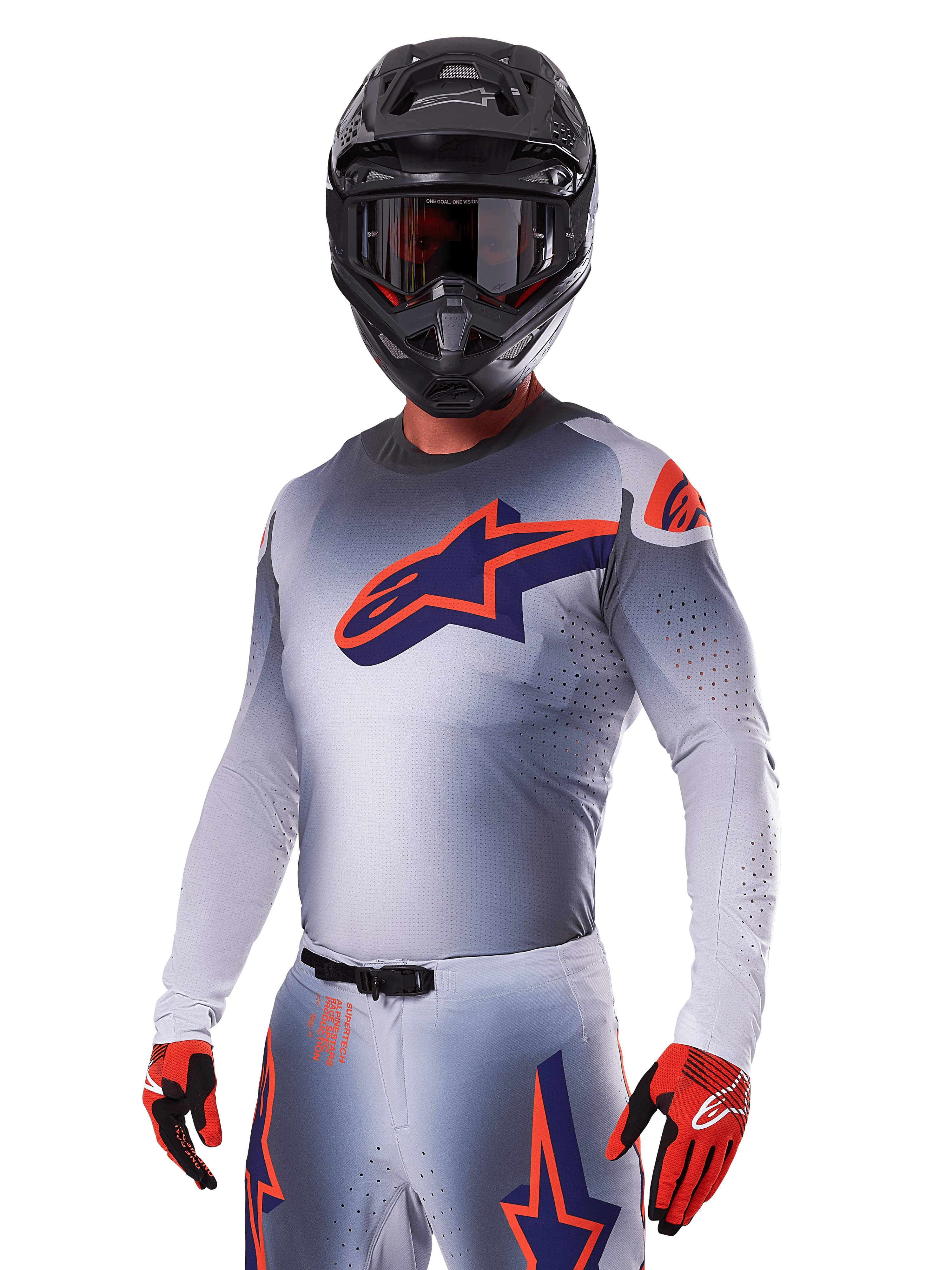 Motocrosskører iført Alpinestars 2025 Supertech Lipan-udstyrssæt, grå jersey og bukser med navy og orange detaljer, mat sort hjelm med goggles og rød-sorte handsker, atletisk præstationsudstyr til terrænkørsel