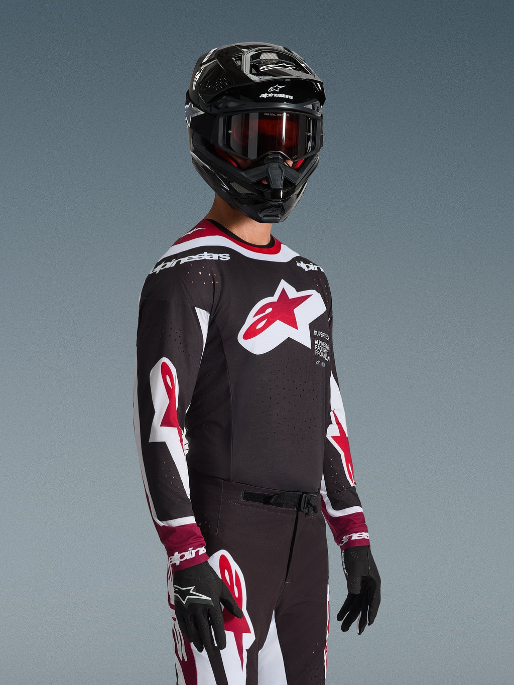 Alpinestars 2026 Supertech AFD Vista Jersey, motocrosskører iført komplet racerudstyr, sort jersey med røde og hvide detaljer, stort logo på brystet, laserskårne perforeringer, båret med matchende bukser, sort hjelm og røde goggles, koordineret outfit til terrænkørsel