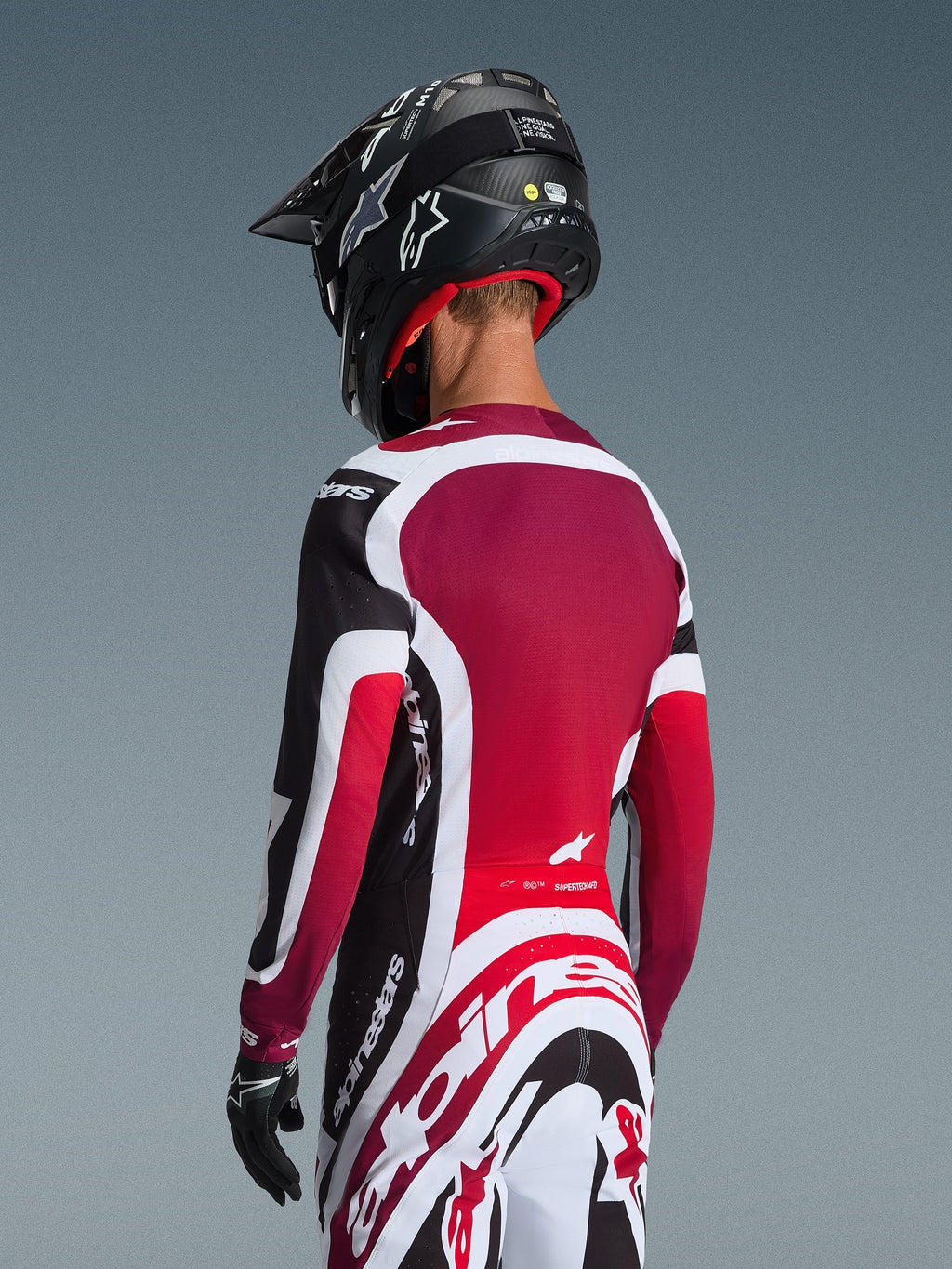 Alpinestars 2026 Supertech AFD Vista-udstyrssæt, rygbillede af en motocrosskører i sort, rødt og hvidt racertøj, trøje med mørkerødt rygpanel og atletisk pasform, matchende bukser med tydeligt Alpinestars-logo, sort hjelm og handsker, professionelt motocross-raceroutfit