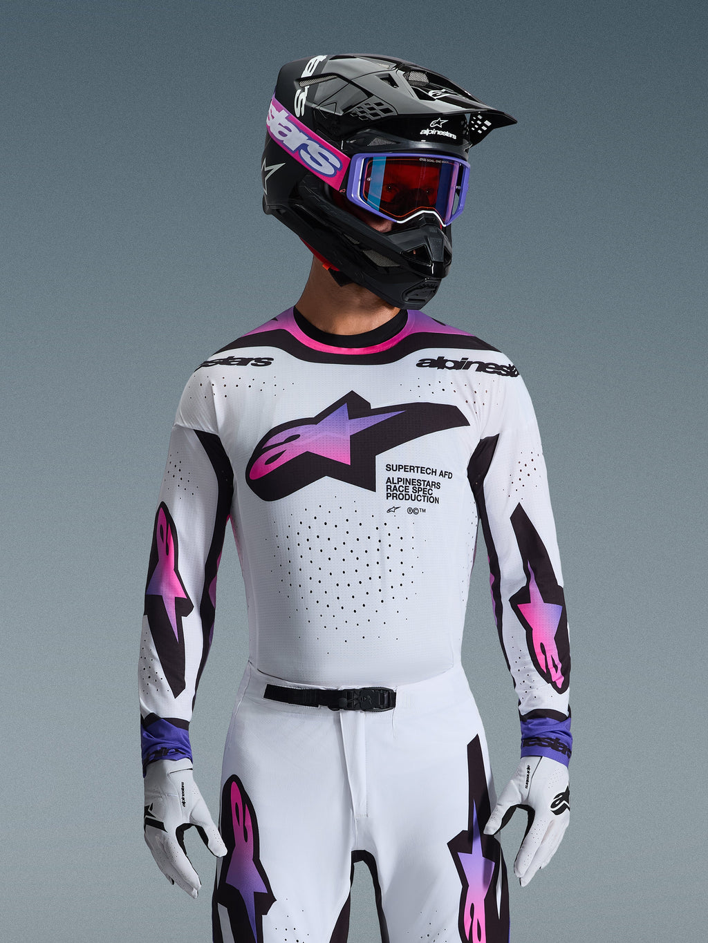 Alpinestars 2026 Supertech AFD Vista-udstyrssæt, professionelt motocross-racerudstyr, hvid trøje og bukser med lyserød og lilla gradientgrafik, sort hjelm med lilla goggles og hvide handsker, atletisk race-pasform til off-road-præstation.