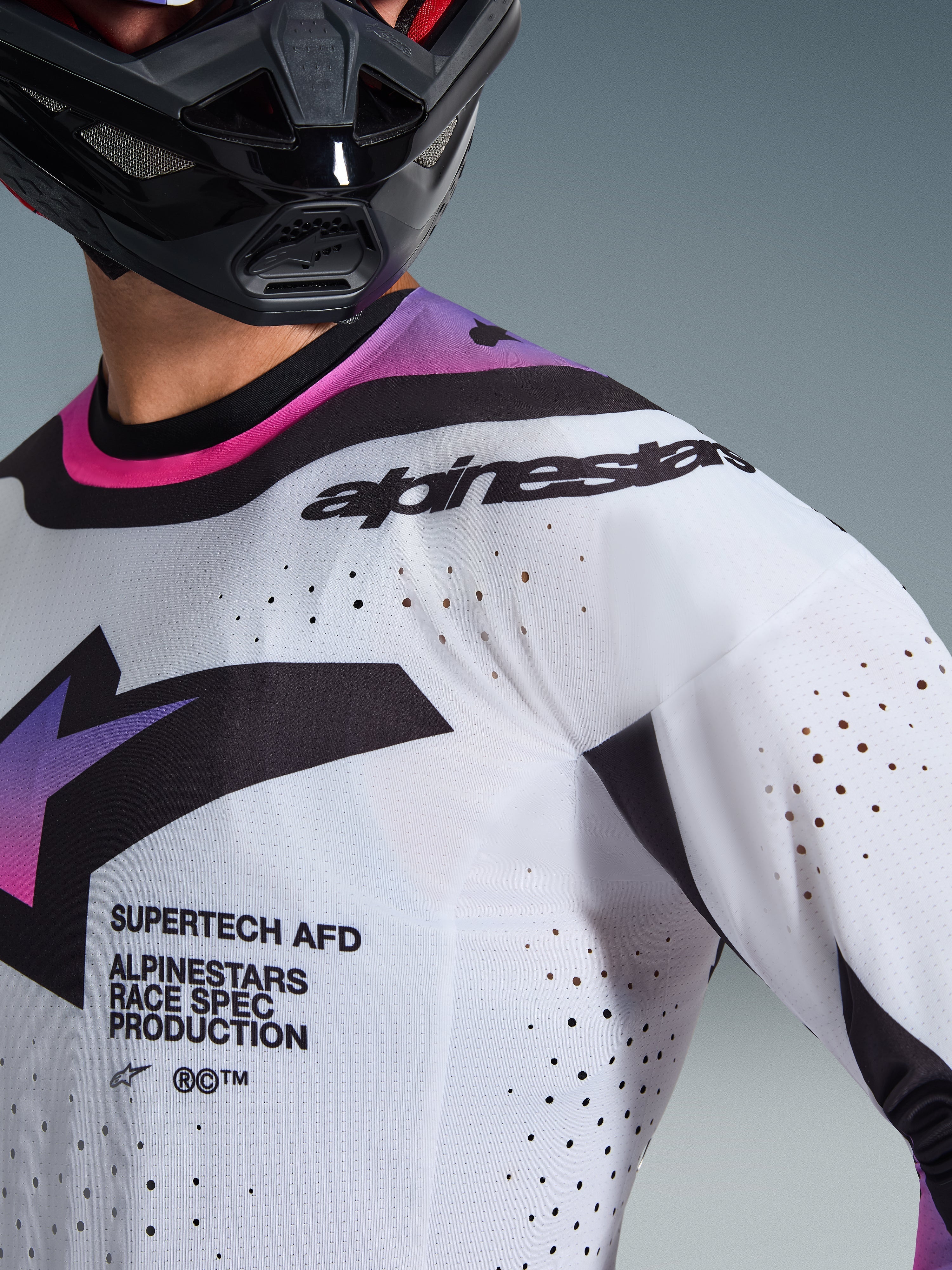 Alpinestars 2026 Supertech AFD Vista Jersey, motocross-trøje, hvid, lilla og sort, nærbillede der viser laserskårne perforeringer og race spec-branding, båret med en sort hjelm, professionelt off-road racerudstyr