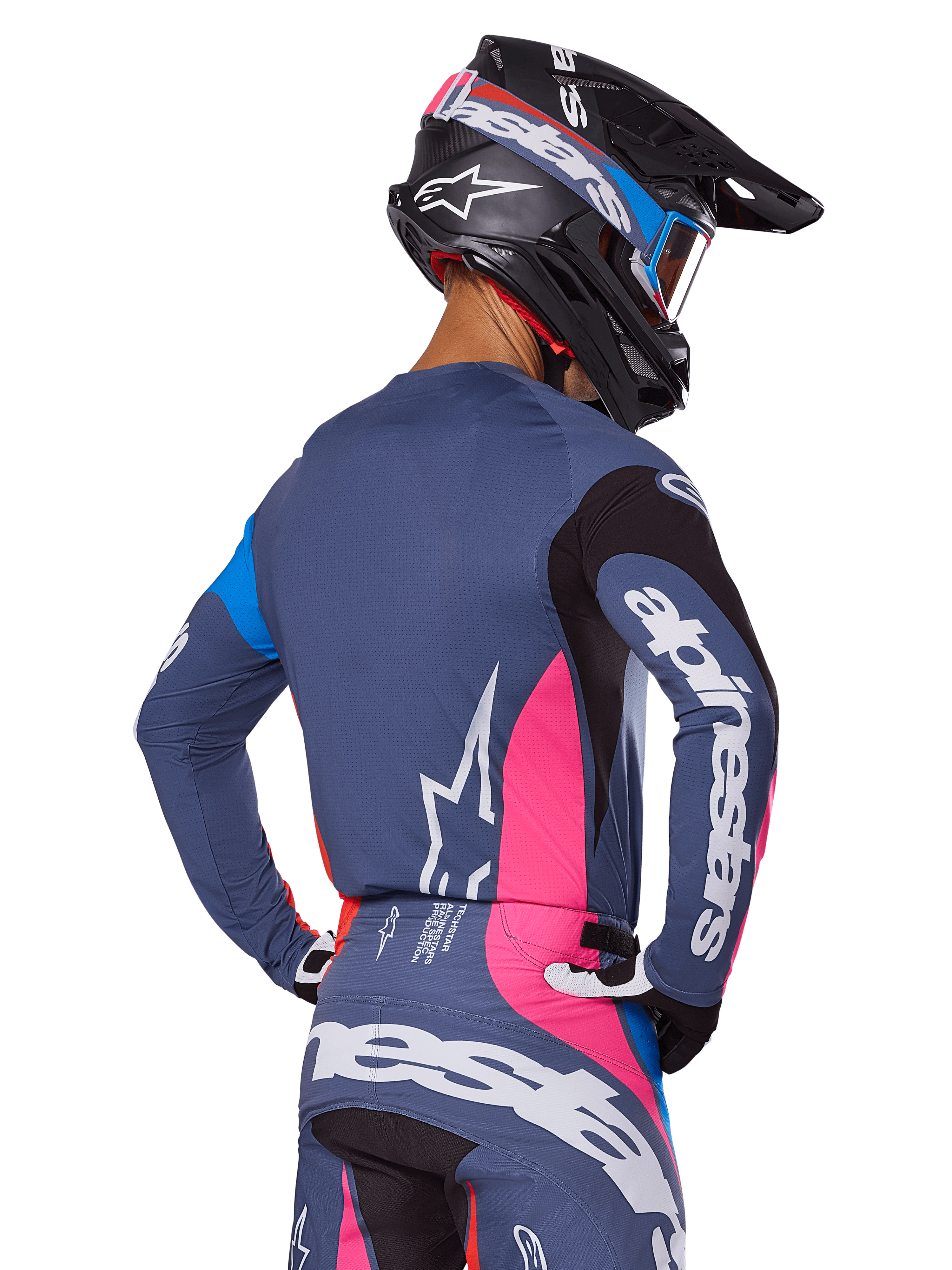 Motocrosskører set bagfra iført Alpinestars 2025 Techstar Dreem-udstyrssættet i grå, bestående af en blågrå jersey og bukser med lyserøde og sorte paneler, hvide Alpinestars-logoer på ærmerne og ryggen samt en matchende sort hjelm med blå og lyserød grafik.
