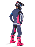 Motocrosskører set bagfra, iført Alpinestars 2025 Techstar Dreem-udstyrssæt, grå med markante lyserøde og hvide detaljer, sort og hvid hjelm og stærkt lyserøde støvler, komplet raceroutfit til motocross-performance.