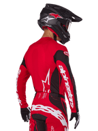 Alpinestars 2025 Techstar Dreem-udstyrssæt, motocross-kører set bagfra, rød og sort jersey med hvidt logo på ærmerne, matchende røde og sorte bukser med markant hvidt logo på bagdelen, sort carbonhjelm med røde detaljer, sort-hvide handsker, professionelt raceroutfit til terrænkørsel