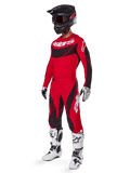 Fuld kropsvisning af en motocross-kører i 2025 Techstar Dreem-udstyrssæt i klar rød og sort, performance-jersey med hvid branding, matchende ripstop-bukser med stræk, sort hjelm med rødt visir, hvide og sorte handsker og hvide Tech-støvler, specialiseret racersæt til off-road-konkurrence