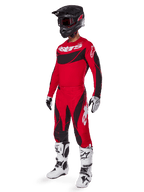 Fuld kropsvisning af en motocross-kører i 2025 Techstar Dreem-udstyrssæt i klar rød og sort, performance-jersey med hvid branding, matchende ripstop-bukser med stræk, sort hjelm med rødt visir, hvide og sorte handsker og hvide Tech-støvler, specialiseret racersæt til off-road-konkurrence