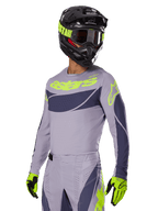 Motocross-kører iført Alpinestars 2025 Techstar Dreem Jersey i grå og mørkegrå, med et neongult 'astars' logo på brystet, kombineret med en matchende hjelm, goggles og handsker for et koordineret off-road racing-look