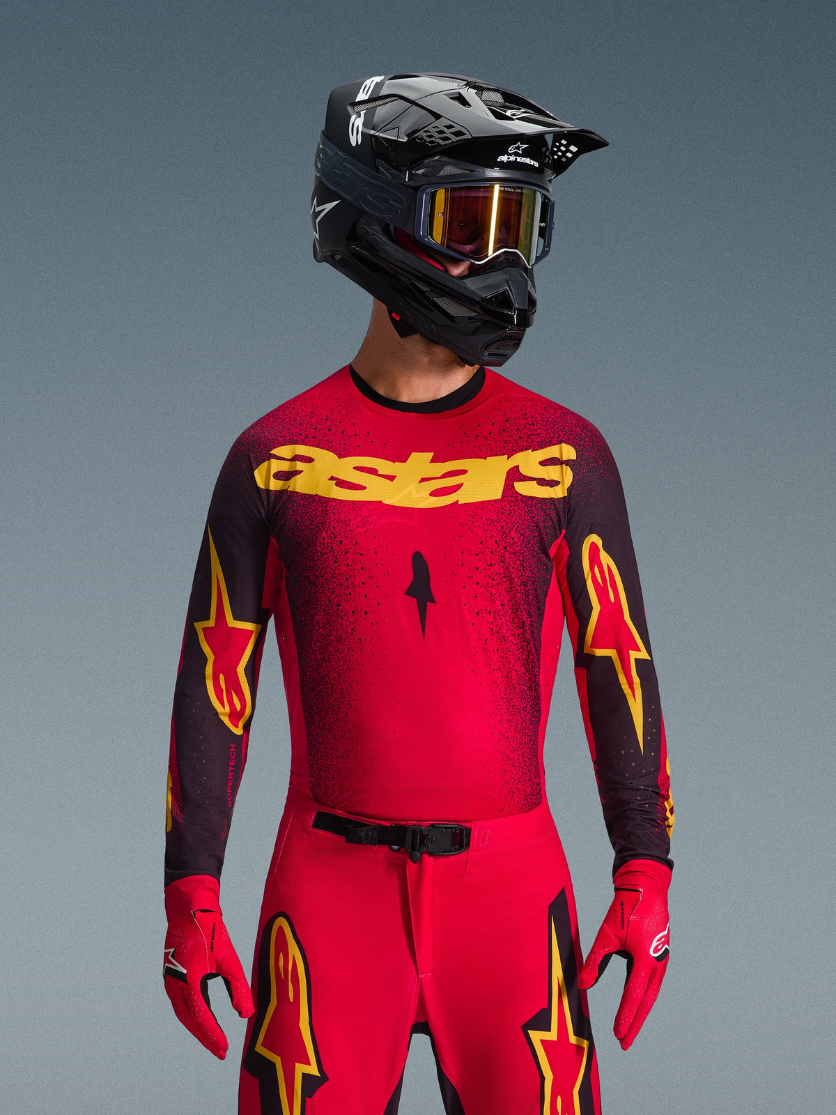 Alpinestars 2026 Supertech Scenz trøje, motocross-trøje, rød, sort og gul, båret af en kører med matchende sort hjelm og røde handsker, med et markant gult 'astars'-logo på brystet og et sort prikket mønster over skuldrene.