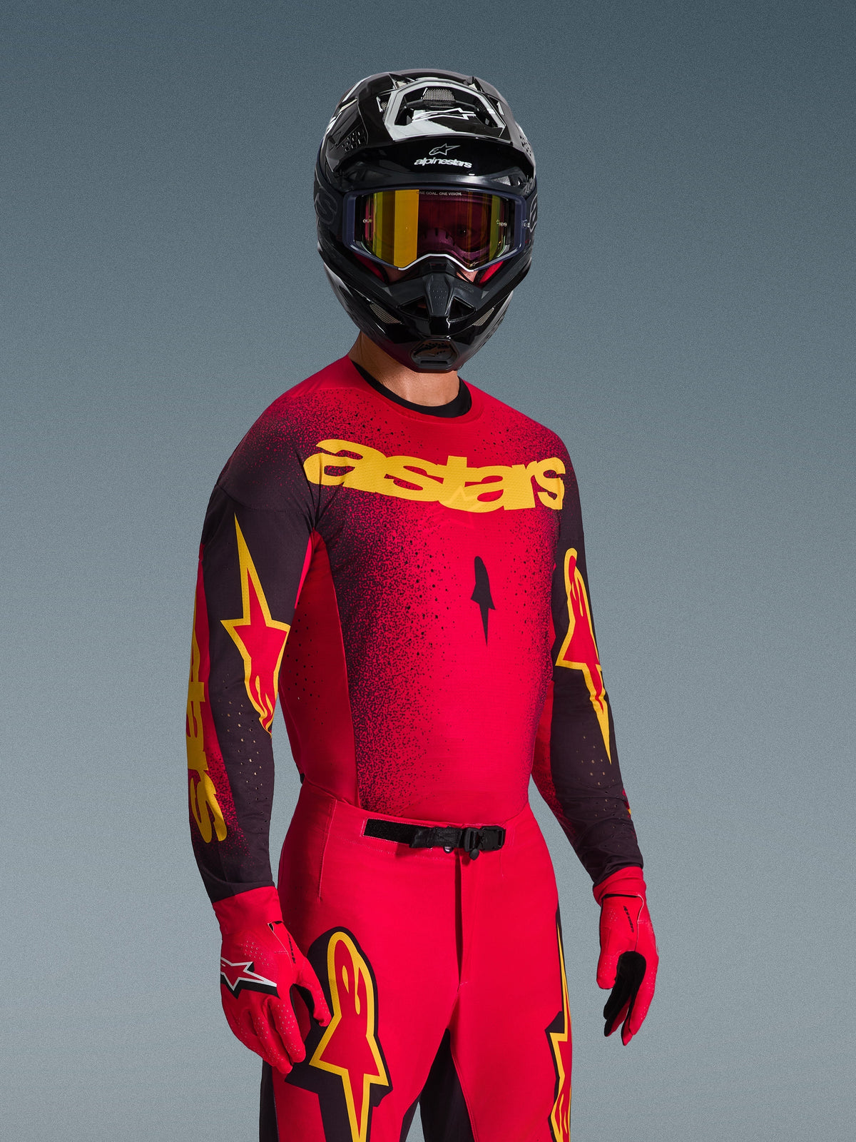 Motocrosskører iført Alpinestars 2026 Supertech Scenz trøje i rød og sort med gul 'astars' branding, matchende røde bukser og handsker, sort hjelm med goggles, professionelt racersæt til off-road motocross