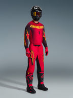 Motocross rider wearing the Alpinestars 2026 Supertech Scenz Jersey in Red Black Yellow, matching red pants with black and yellow accents, black helmet with goggles, red gloves, and black boots with red details, complete professional racing gear set.