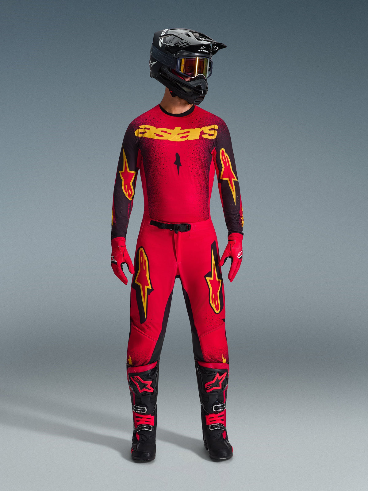 Motocross-kører iført Alpinestars 2026 Supertech Scenz-trøje i rød, sort og gul, kombineret med matchende bukser, sort hjelm med goggles, røde handsker og sort-røde støvler, professionelt racersæt til terrænkørsel