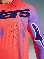 Alpinestars 2026 Supertech Scenz Jersey, motocross-trøje, Hot Coral og lilla, nærbillede der viser åndbar mesh-tekstur og laser-skårne perforeringer, med stort lilla brystlogo og grafik på ærmerne til professionel terrænkørsel.