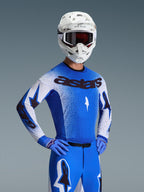 Alpinestars 2026 Supertech Scenz jersey, motocross-jersey, Ucla Blue og hvid, båret som et komplet udstyrssæt med matchende blå bukser og handsker, med sort 'astars' branding, hvid hjelm og mørke briller, professionel atletisk racerpasform.