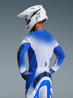 Motocross-kører iført Alpinestars 2026 Supertech Scenz-trøje i Ucla Blue White, set bagfra, koordineret med matchende racerbukser og en hvid Alpinestars-hjelm, professionelt terrænkørselsudstyr
