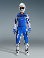 Motocrosskører iført Alpinestars 2026 Supertech Scenz-udstyrssæt i Ucla Blue og hvid, bestående af en let blå og hvid trøje med sorte logoer, matchende blå bukser, hvid racerhjelm og hvide motocrossstøvler, professionelt performance-udstyr til terrænkørsel.