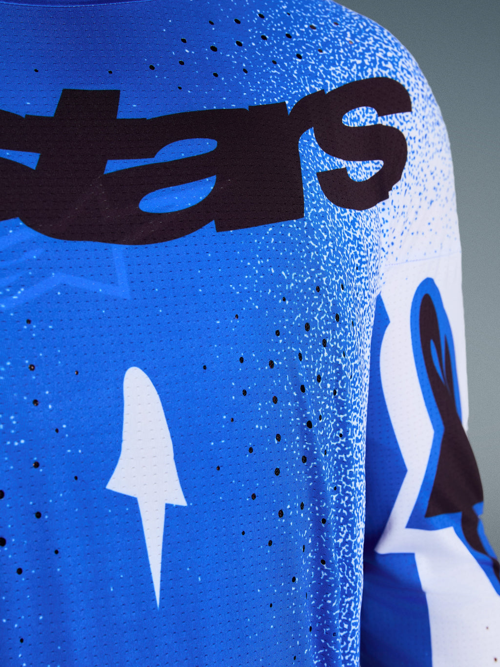 Alpinestars 2026 Supertech Scenz Jersey, nærbillede af Ucla Blue og hvidt design, laserskårne perforeringer til ventilation, sort 'stars' branding, åndbart mesh-stof til professionel motocross-racing