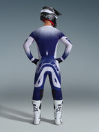 Alpinestars 2026 Supertech Scenz-udstyrssæt, set bagfra af en motocross-kører i blå og hvid racing-jersey og bukser, prikket gradienteffekt, båret med hvide motocrossstøvler og sort hjelm, professionelt udstyr til terrænkørsel