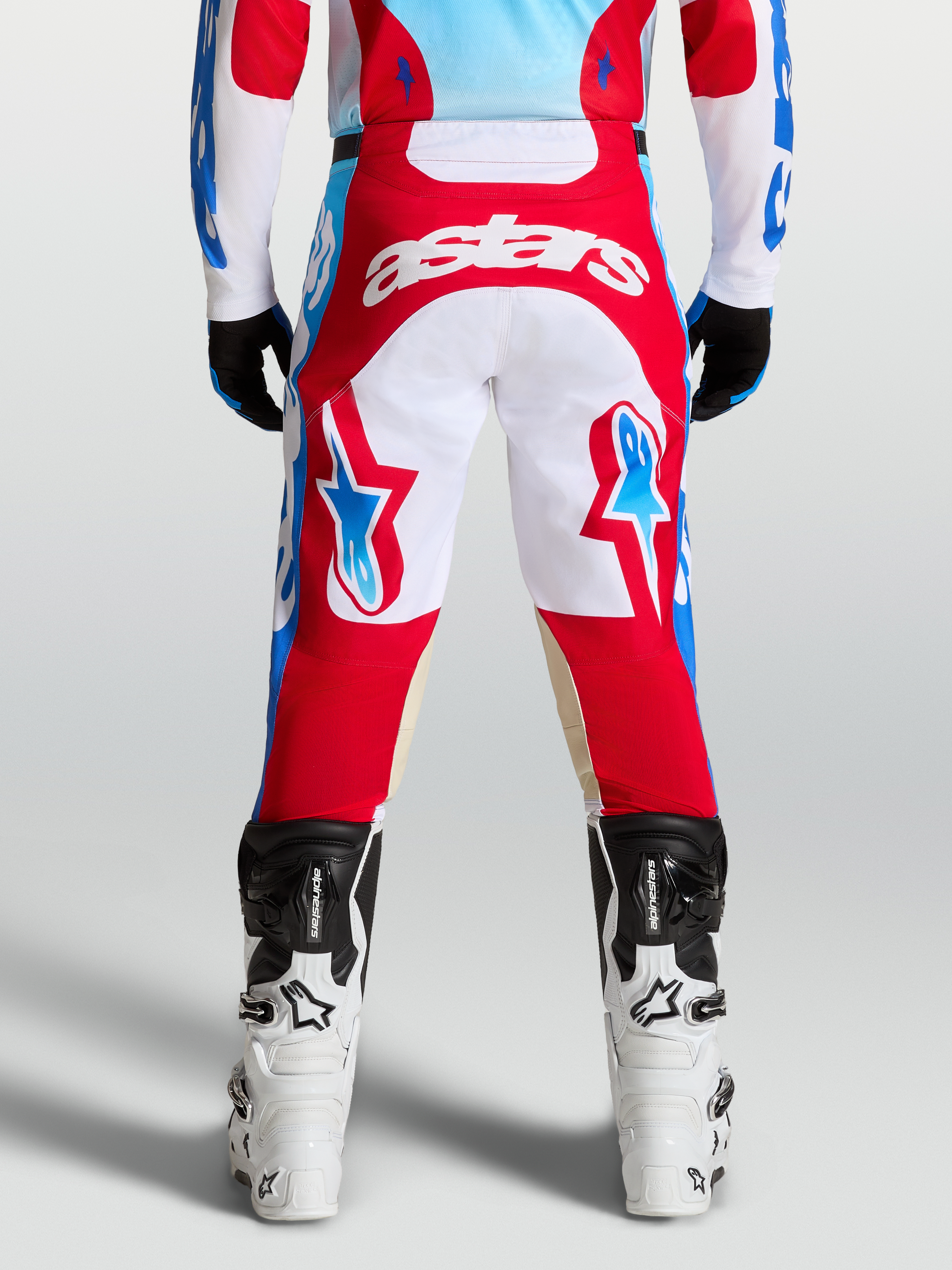 Alpinestars Racer Hunt Bukser, røde og hvide motocrossbukser set bagfra på en rytter, med lyseblå detaljer og ergonomisk forbuet benkonstruktion.