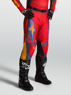 Alpinestars Racer Hunt bukser, rød motocrossbukser til mænd med grå og orange detaljer, vist på model med sorte støvler.