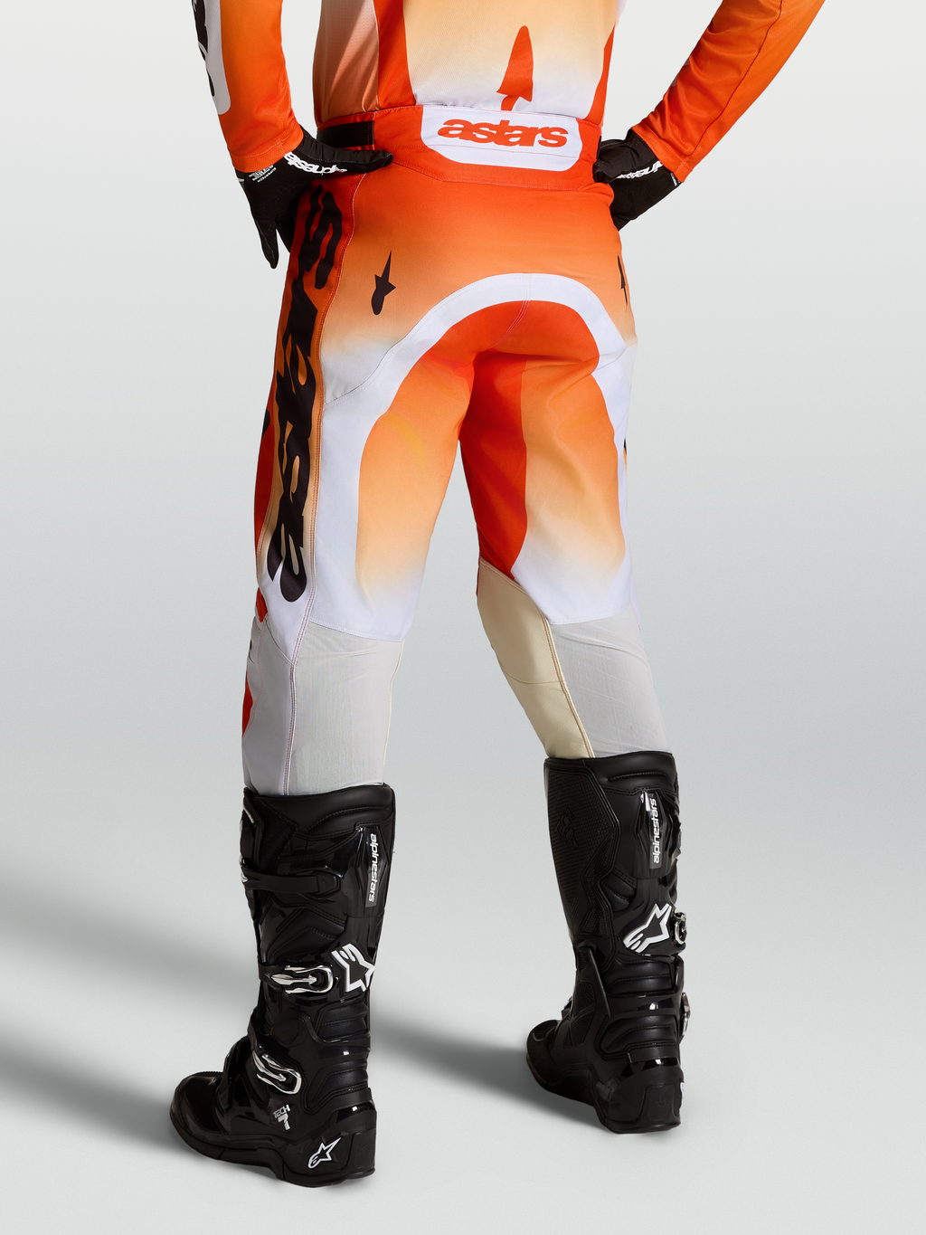 Alpinestars Racer Amber bukser, orange og hvide motocrossbukser til mænd, set bagfra med sorte motocrossstøvler, slidstærkt 600D polyfabric, off-road racing