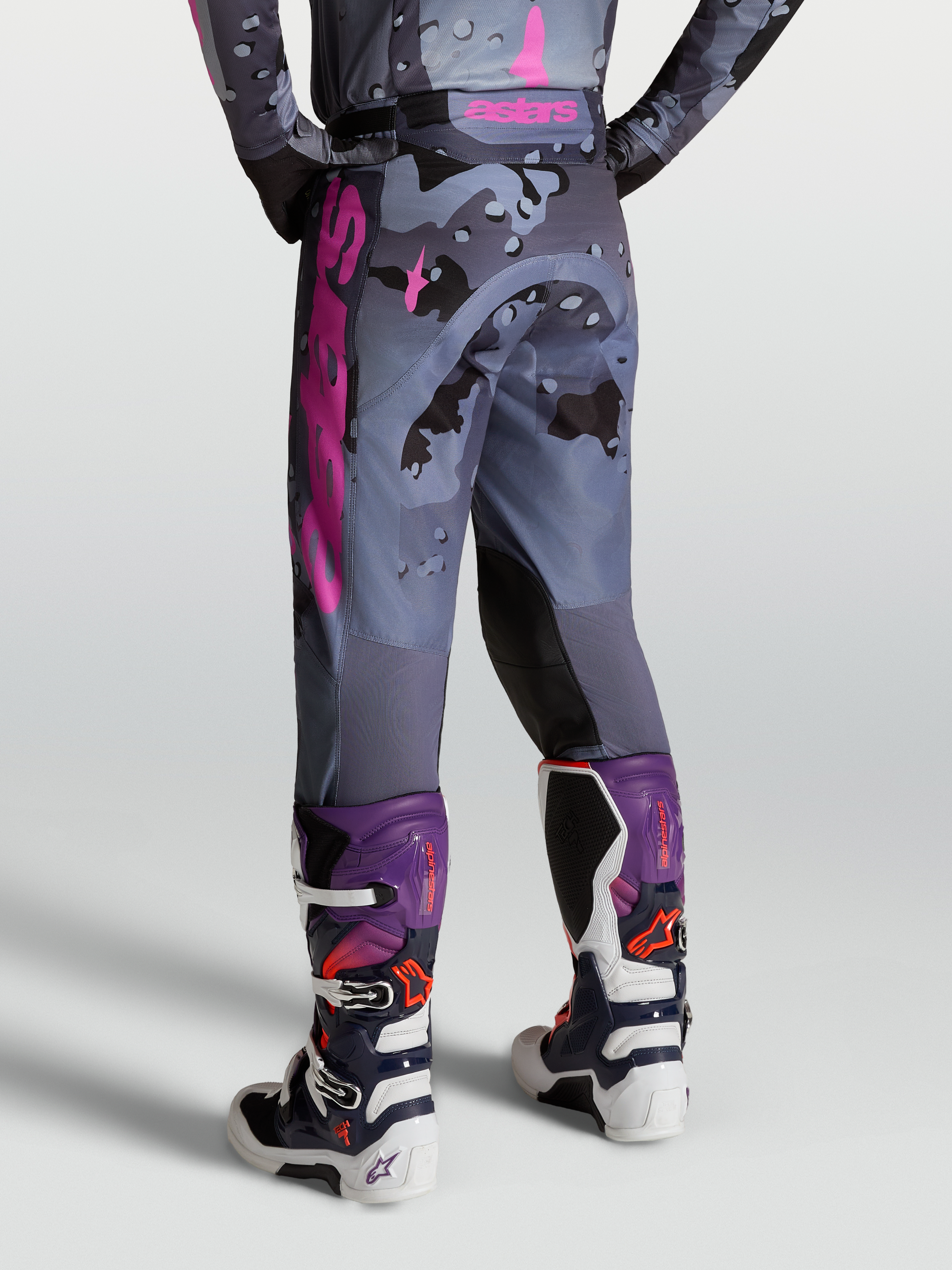 Alpinestars Racer Lone Bukser, motocrossbukser i grå camouflage og lilla, set bagfra på model med Tech 7 støvler, slidstærkt materiale til terrænkørsel.