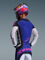 Motocrosskører set bagfra iført 2026 Techstar Knif Jersey, sort, lysegrå og lilla, med hvide perforerede ærmer og lyserøde Alpinestars-logoer, matchende lilla og lyserød hjelm, professionelt off-road racerudstyr.