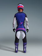 Alpinestars 2026 Techstar Knif Jersey, set bagfra af en motocross-kører i sort, lysegrå og lilla, hvide ærmer og lyserødt logo på ryggen, matchende motocross-bukser, lilla støvler og farverig hjelm i et studiemiljø.