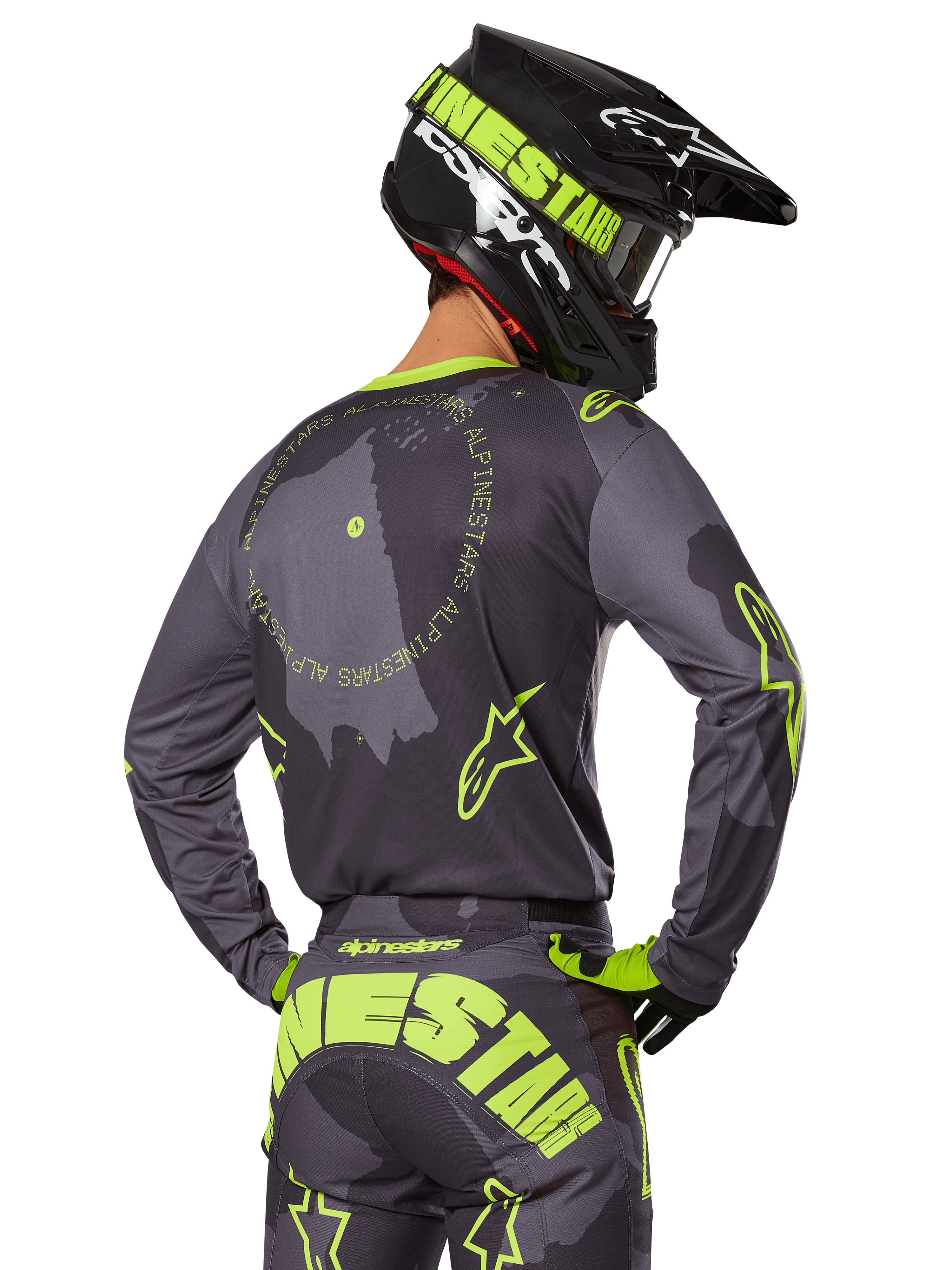 Alpinestars 2025 Racer Hollow Gear Set, motocross-kører set bagfra, grå trøje med fluorescerende gul cirkulær tekst og stjernelogoer, matchende grå og gule bukser med iøjnefaldende branding over sædet, sort og limegrøn hjelm, koordineret outfit til off-road racing