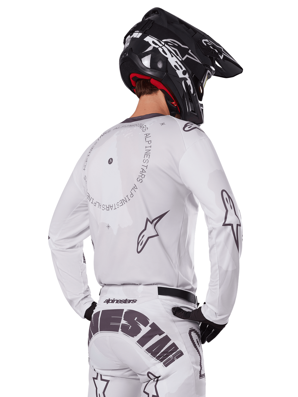 Motocrosskører set bagfra iført Alpinestars 2025 Racer Hollow udstyrssæt i hvid, hvid langærmet trøje med grå stjernelogoer og cirkulær grafik, matchende hvide bukser med markant branding på sædet, sort hjelm, koordineret off-road racingudstyr.