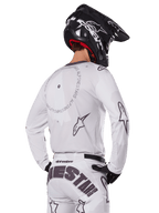 Motocrosskører set bagfra iført Alpinestars 2025 Racer Hollow udstyrssæt i hvid, hvid langærmet trøje med grå stjernelogoer og cirkulær grafik, matchende hvide bukser med markant branding på sædet, sort hjelm, koordineret off-road racingudstyr.