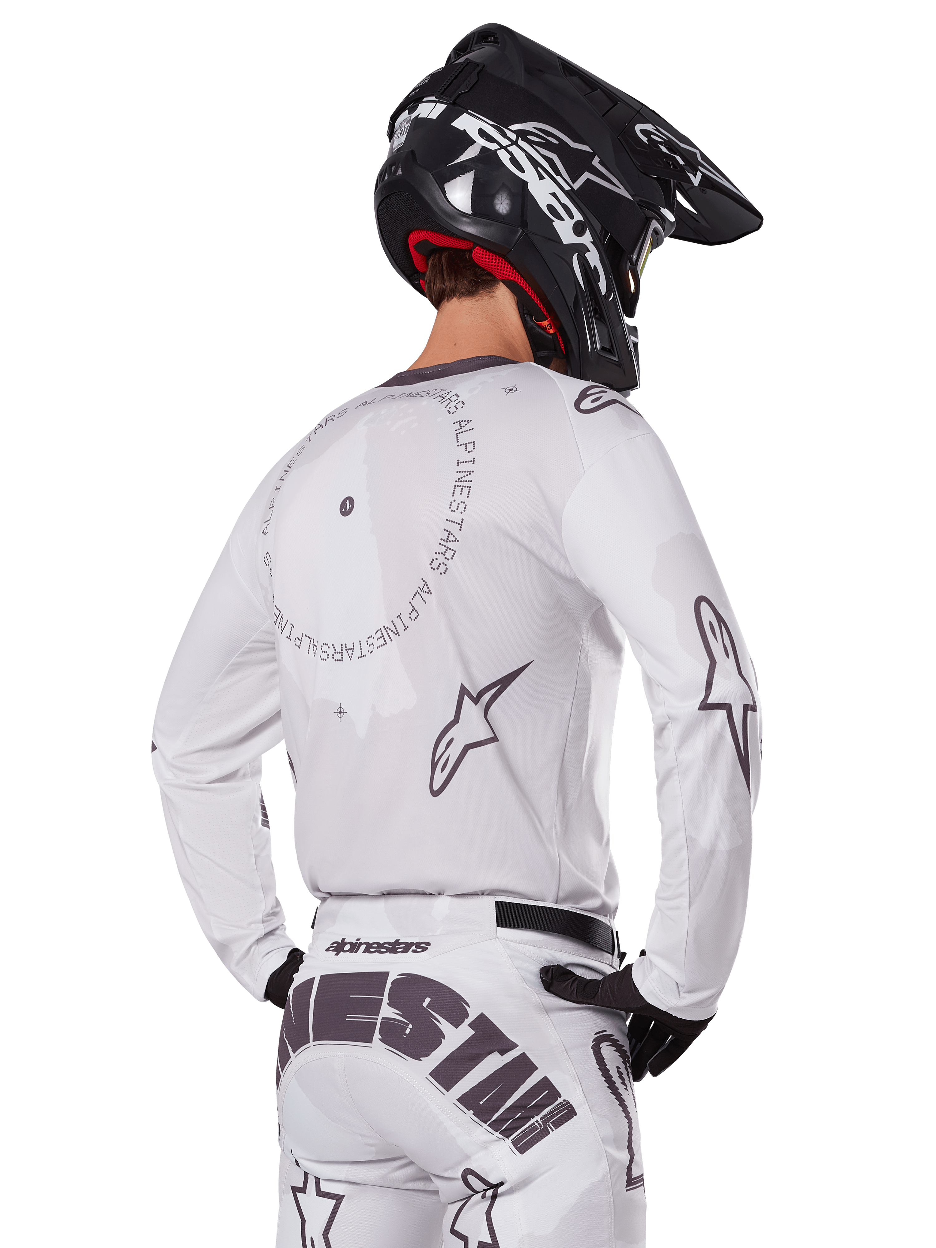 Motocrosskører set bagfra iført Alpinestars 2025 Racer Hollow udstyrssæt i hvid, hvid langærmet trøje med grå stjernelogoer og cirkulær grafik, matchende hvide bukser med markant branding på sædet, sort hjelm, koordineret off-road racingudstyr.