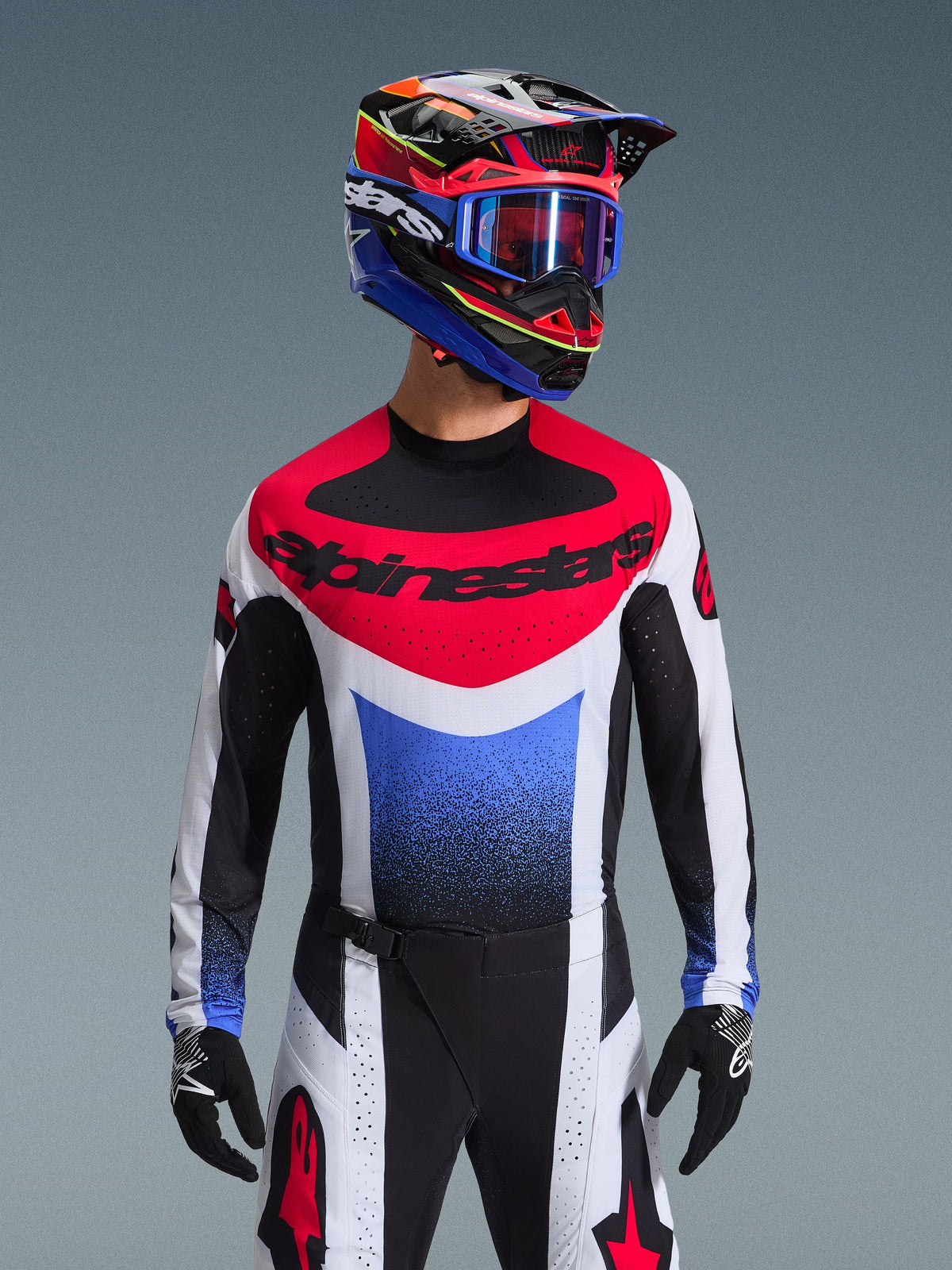 Alpinestars 2026 Techstar Knif trøje, motocross trøje, rød, hvid og blå, med et markant brystlogo og gradient på torsoen, båret af en kører med en matchende multifarvet hjelm, blå goggles og sorte handsker, professionelt off-road racerudstyr.