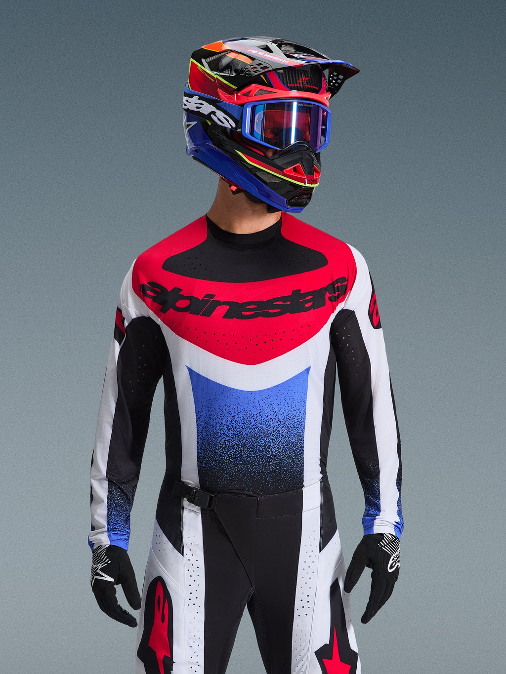 Alpinestars 2026 Techstar Knif trøje, motocross trøje, rød, hvid og blå, med et markant brystlogo og gradient på torsoen, båret af en kører med en matchende multifarvet hjelm, blå goggles og sorte handsker, professionelt off-road racerudstyr.