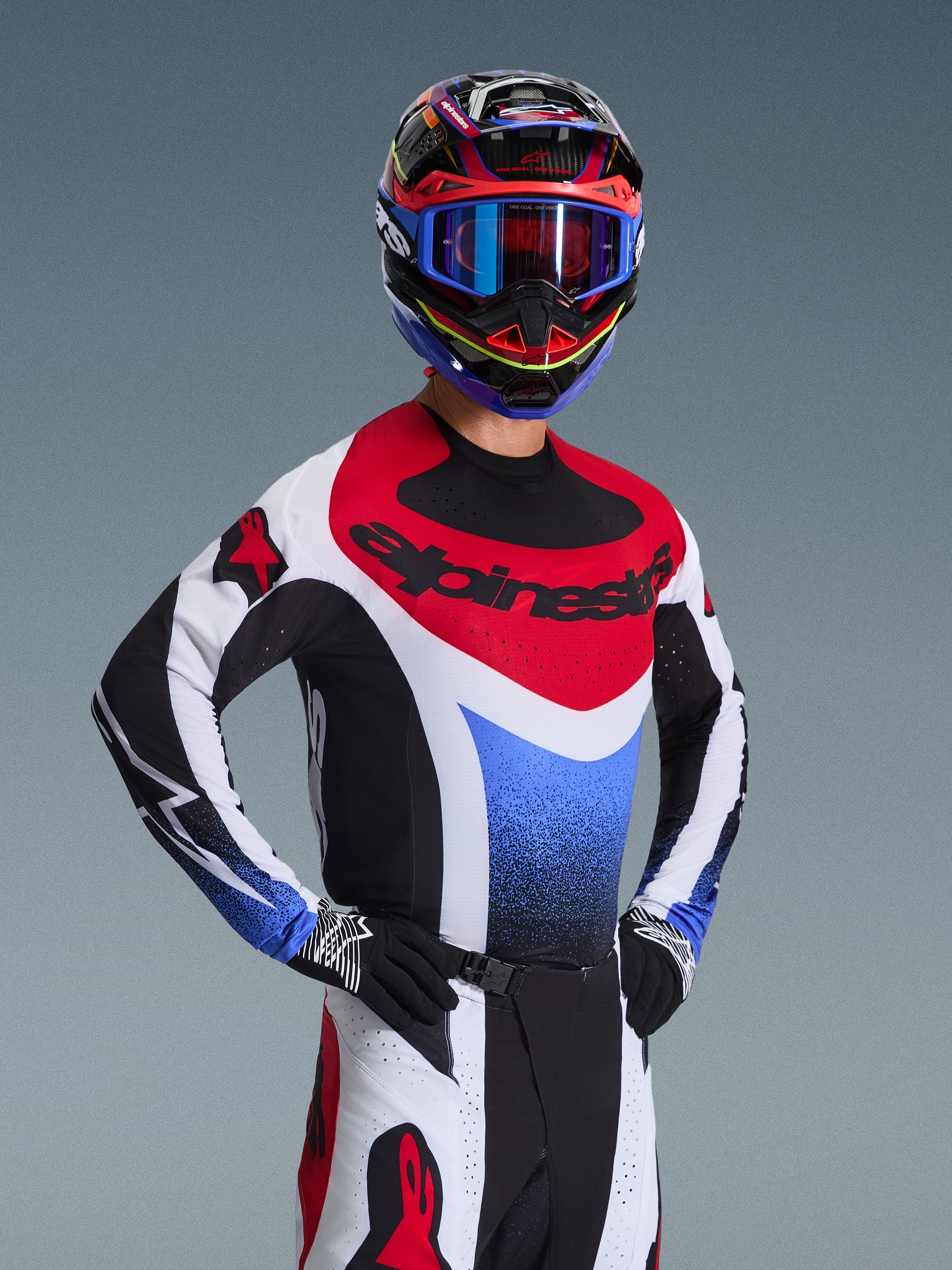 Motocrosskører iført Alpinestars 2026 Techstar Knif-trøje i rød, hvid og blå, med sort branding på brystet, kombineret med matchende motocrossbukser, en koordineret racerhjelm med blå goggles og sort-hvide handsker, professionelt off-road-udstyr til konkurrence