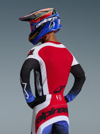 Alpinestars 2026 Techstar Knif-udstyrssæt, motocross-rytter set bagfra, rød trøje med hvide sidepaneler, sorte ærmer med blåspættede manchetter, røde og hvide bukser med sort Alpinestars-branding over sædet, matchende blå og rød hjelm med goggles