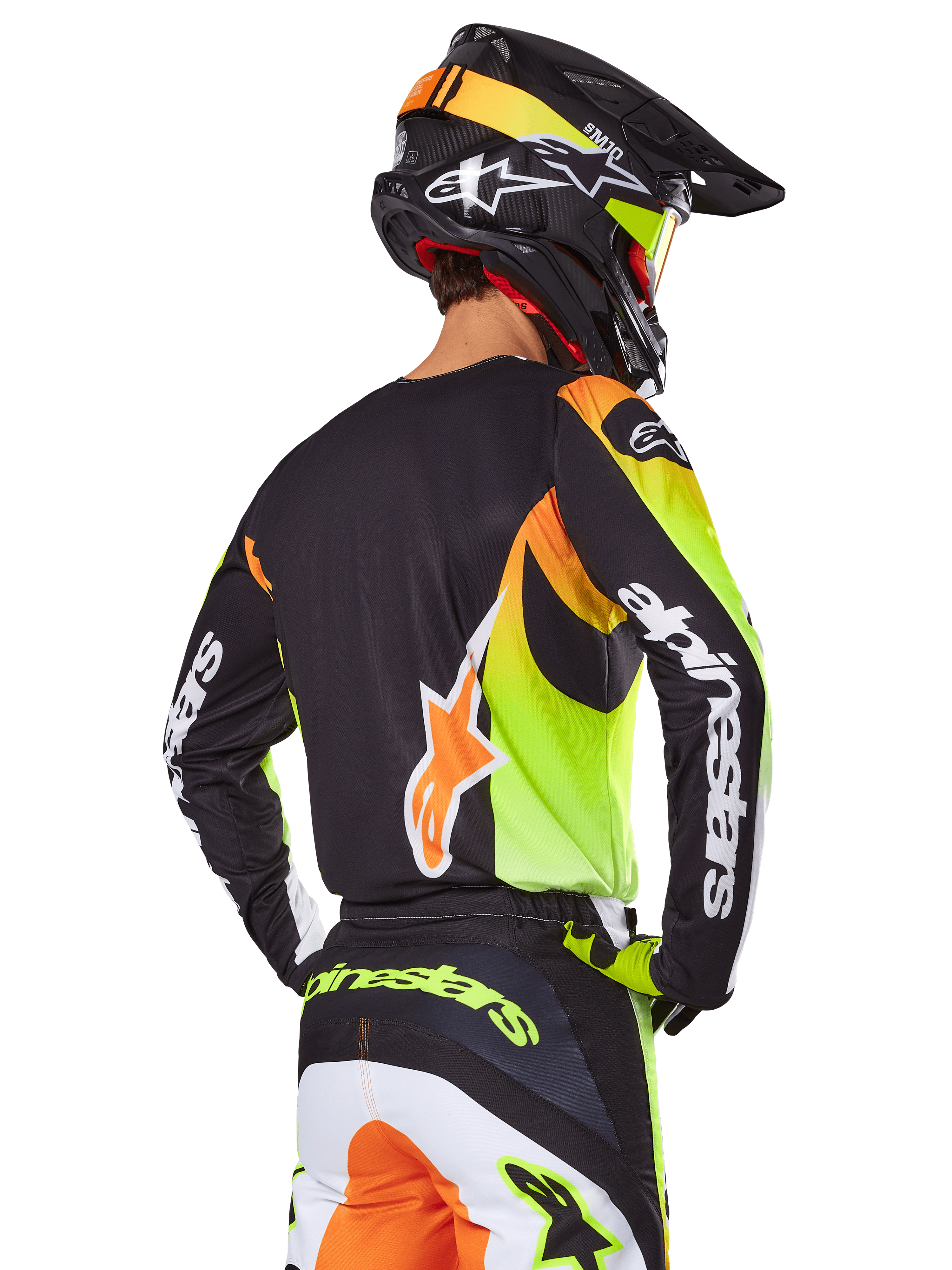 Motocrosskører set bagfra iført Alpinestars 2025 Fluid Wurx-udstyrssæt, sort trøje med neongul og orange grafik, matchende bukser med hvide og orange paneler, sort hjelm med neon-detaljer, tydelig Alpinestars-branding på ærmer og bagpå