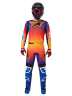 Motocrossrytter iført Alpinestars 2025 Fluid Wurx-udstyrssæt, med en livlig orange, gul og blå gradient på trøjen og bukserne, sorte Alpinestars-logoer, kombineret med blå racestøvler, røde og sorte handsker og en sort hjelm med røde goggles, komplet koordineret outfit til off-road racing