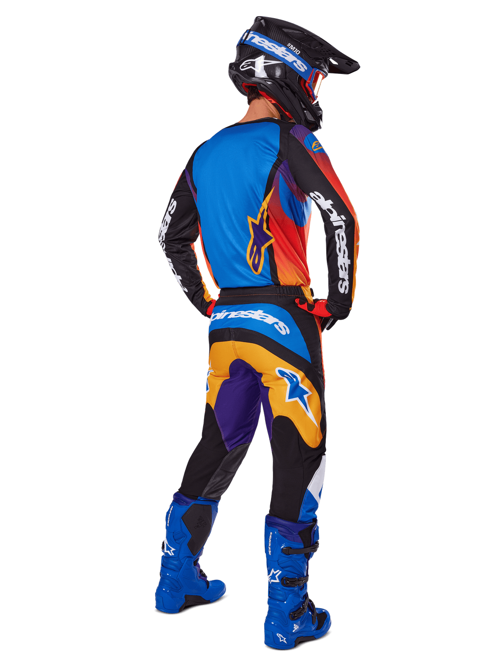 Motocross-rytter set bagfra iført Alpinestars 2025 Fluid Wurx-udstyrssæt, flerfarvet trøje med blå, orange og lilla paneler, matchende bukser med hvidt Alpinestars-logo på sædet, klare blå støvler og en sort hjelm, koordineret outfit til off-road racing