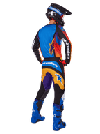 Motocross-rytter set bagfra iført Alpinestars 2025 Fluid Wurx-udstyrssæt, flerfarvet trøje med blå, orange og lilla paneler, matchende bukser med hvidt Alpinestars-logo på sædet, klare blå støvler og en sort hjelm, koordineret outfit til off-road racing