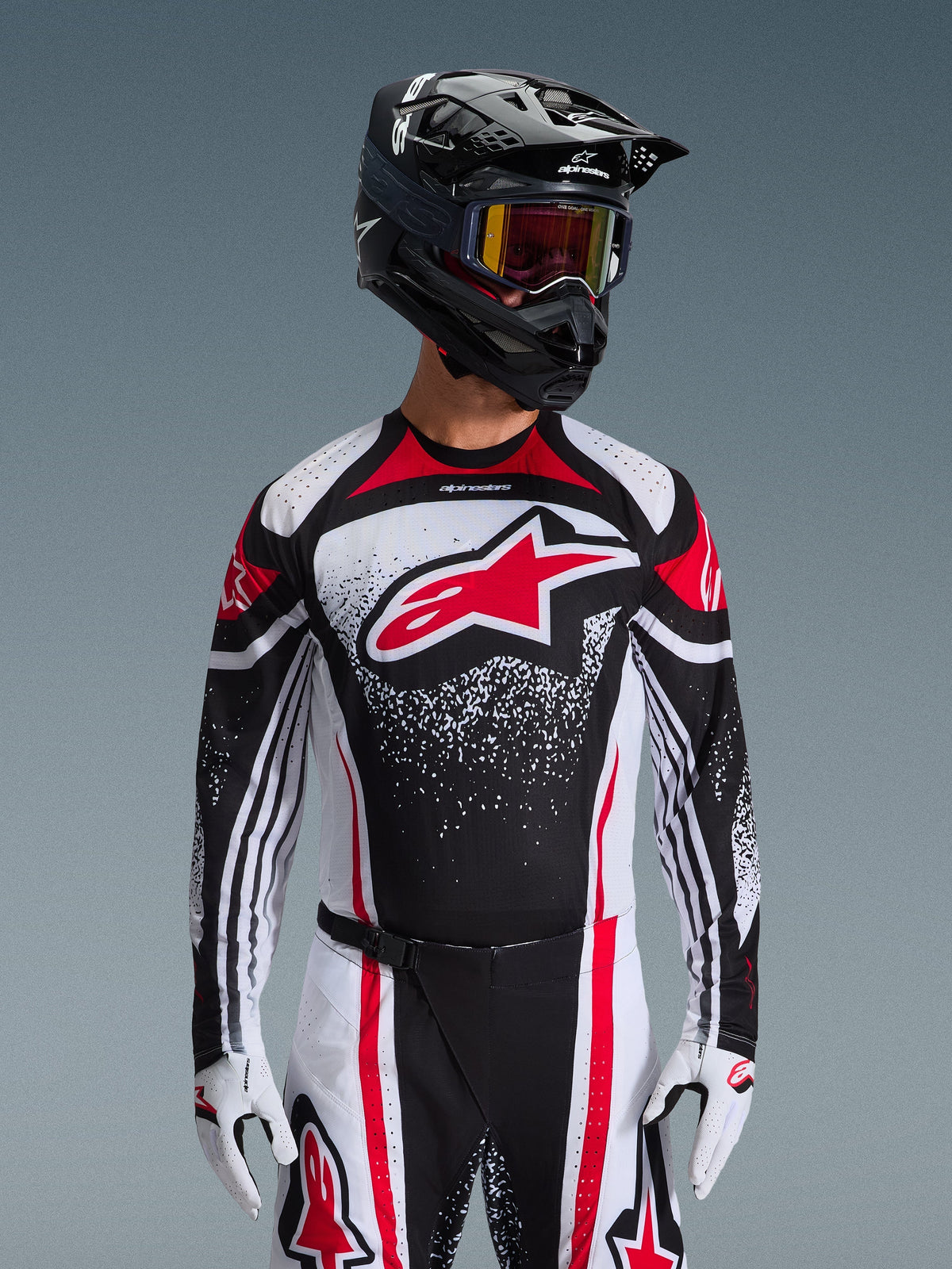 Alpinestars 2026 Techstar Nomur jersey, motocross-trøje, sort, hvid og rød, båret af en kører med matchende bukser, sort hjelm og hvide handsker, med et stort rødt Astars-logo og spættet grafisk design, atletisk race fit til off-road-konkurrence