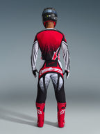 Alpinestars 2026 Techstar Nomur-trøje, motocrossrytter set bagfra, rød, sort og hvid med spættet mønster, matchende racerbukser, røde motocrossstøvler og sort hjelm, komplet udstyrssæt til off-road konkurrence
